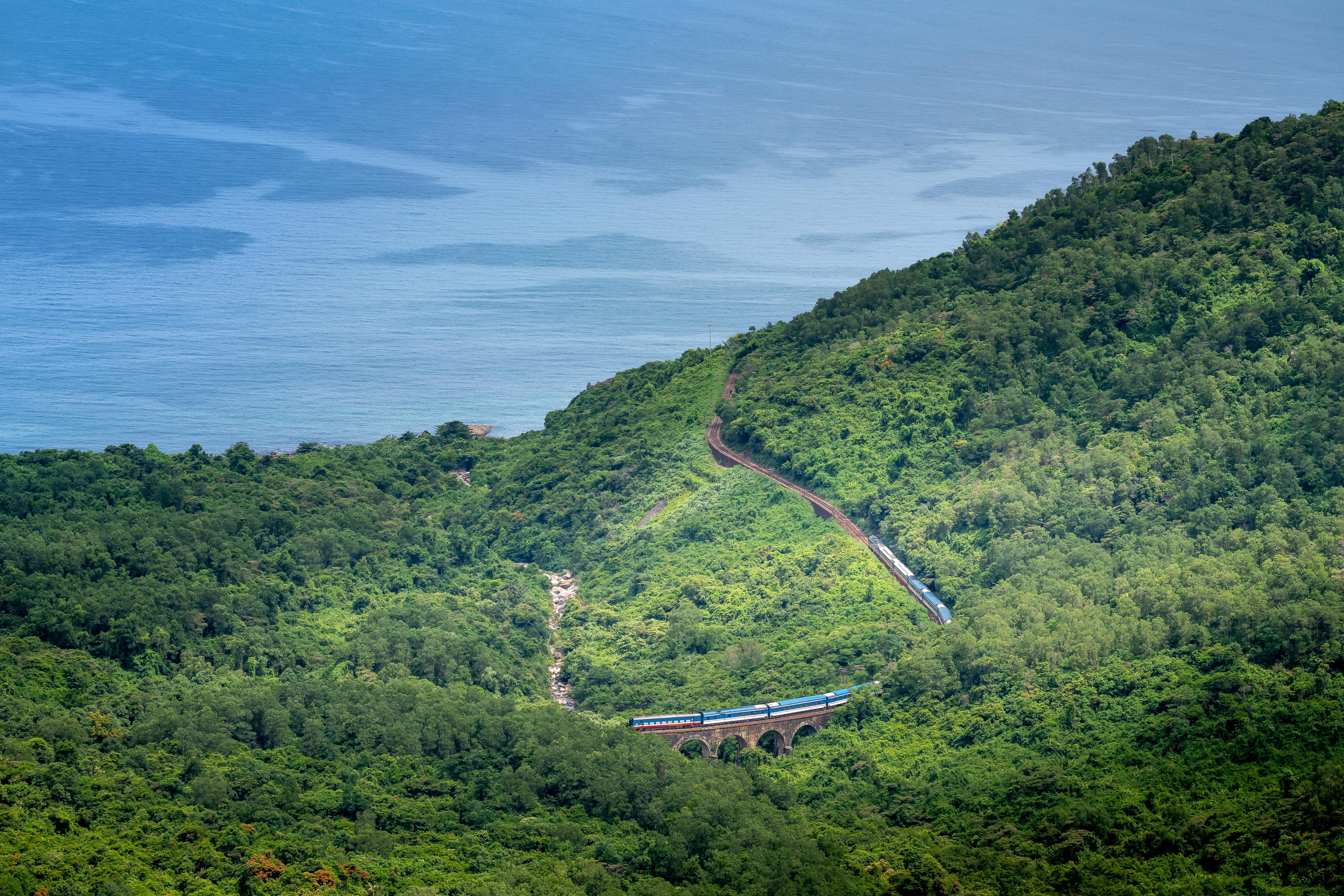 Vietnamese train on a stone viaduct crossing the green hillside above the sea