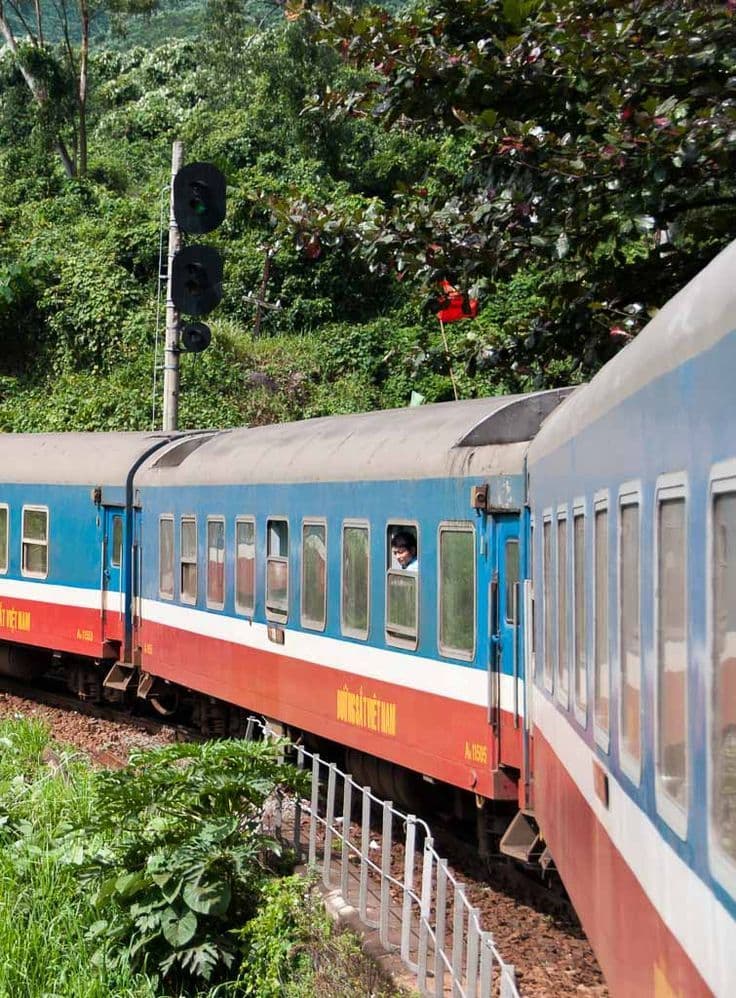 Blue and red Vietnamese Railways carriages passing through tropical greenery
